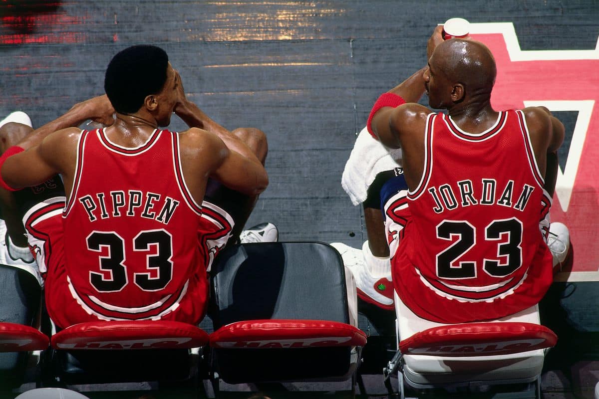 Michael Jordan and Scottie Pippen sitting next to each other on the bench on the court Red Black the Bulls